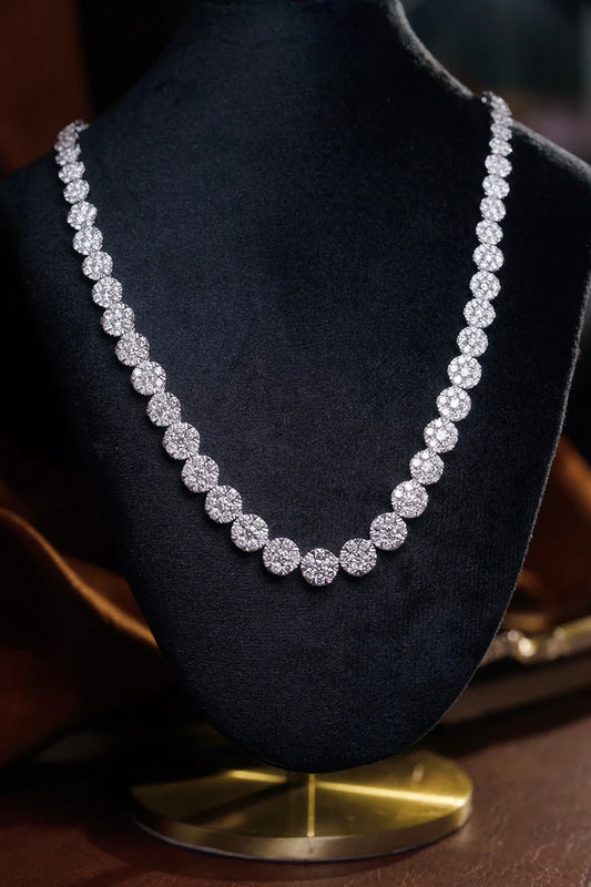 A sparkling diamond tennis necklace displayed on a black velvet jewelry bust with a gold base, set against a dark background.