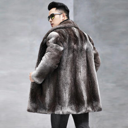 A man wearing a dark brown and gray faux fur coat, black sunglasses, and black pants, photographed from the back against a gray concrete wall.