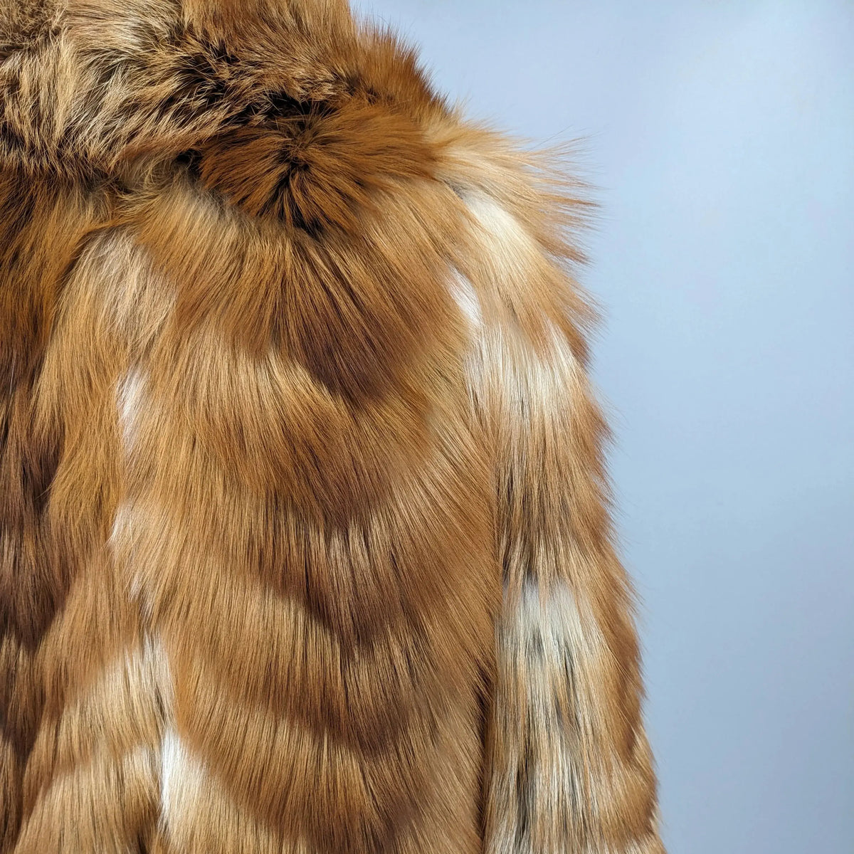 Close-up of a brown and cream patterned faux fur garment, showing the texture and color details against a solid light blue background.