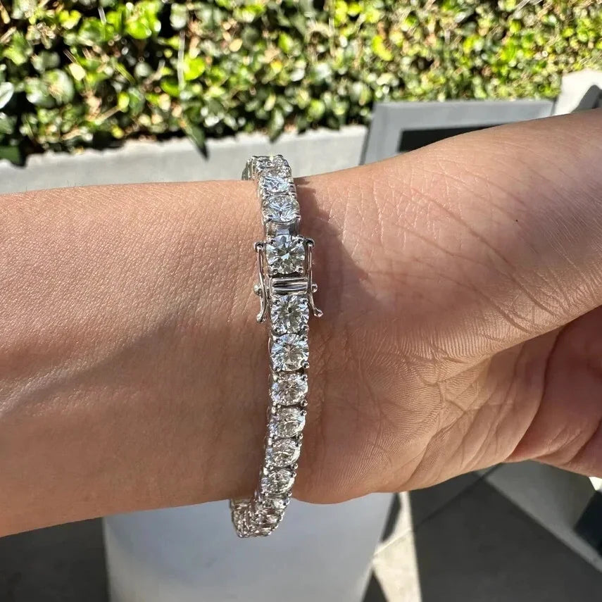 A silver tennis bracelet with baguette-cut clear stones worn on a person's wrist, photographed outdoors with green foliage in the background.