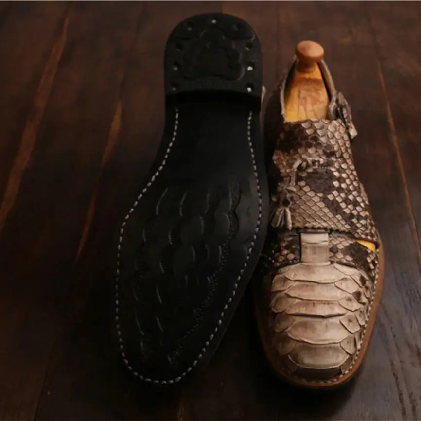 A pair of men's dress shoes displayed on a dark wooden surface, showing both the black leather outsole and the textured snakeskin-patterned upper.