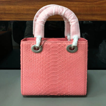 A pink textured handbag with a snakeskin pattern, featuring two rolled top handles wrapped in white protective material and silver-tone hardware, set against a dark background.