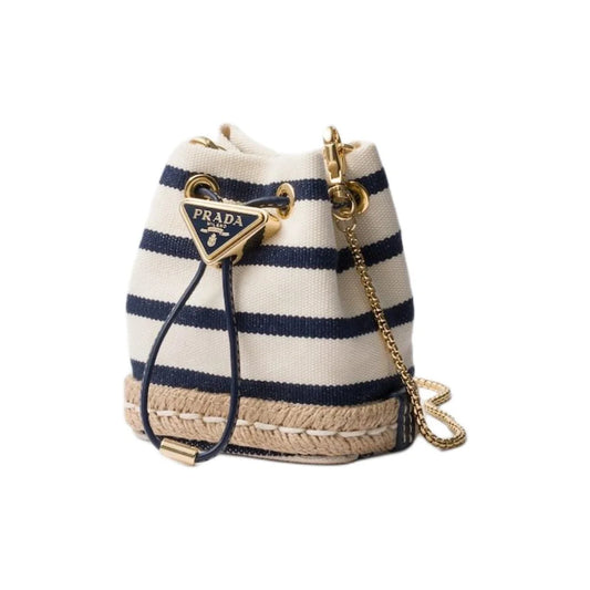 Prada canvas bucket bag with navy and cream horizontal stripes, a beige jute-wrapped base, a gold-tone triangular Prada logo charm, and a gold chain strap on a white background.
