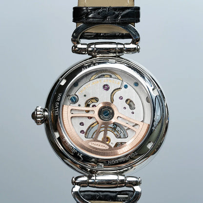 Close-up of a mechanical watch with visible brand name on a light gray background