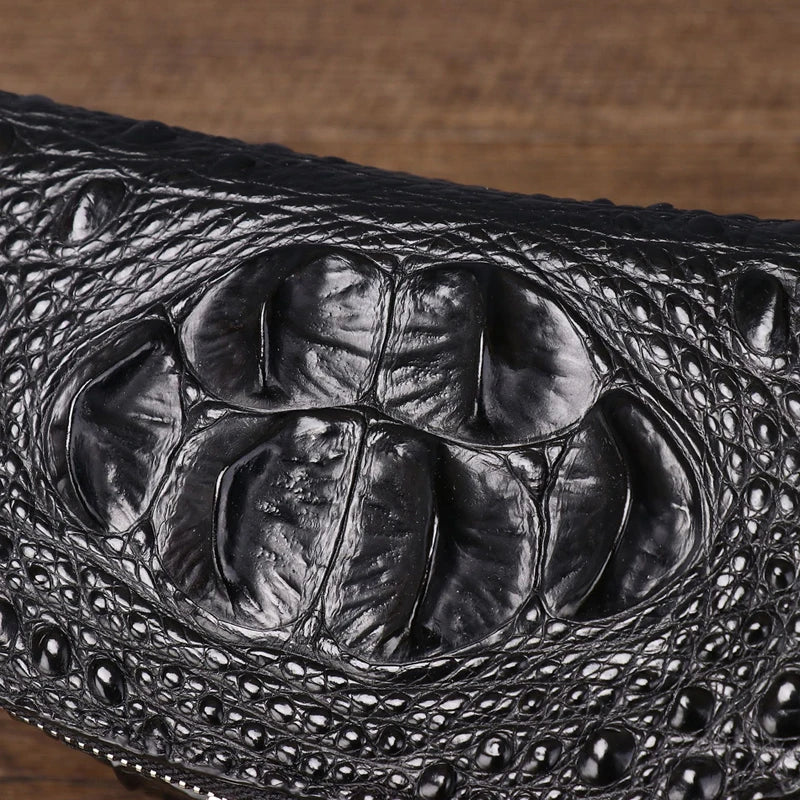 Close-up of a black crocodile-embossed leather item, showing glossy textured scales and a wood surface in the background.