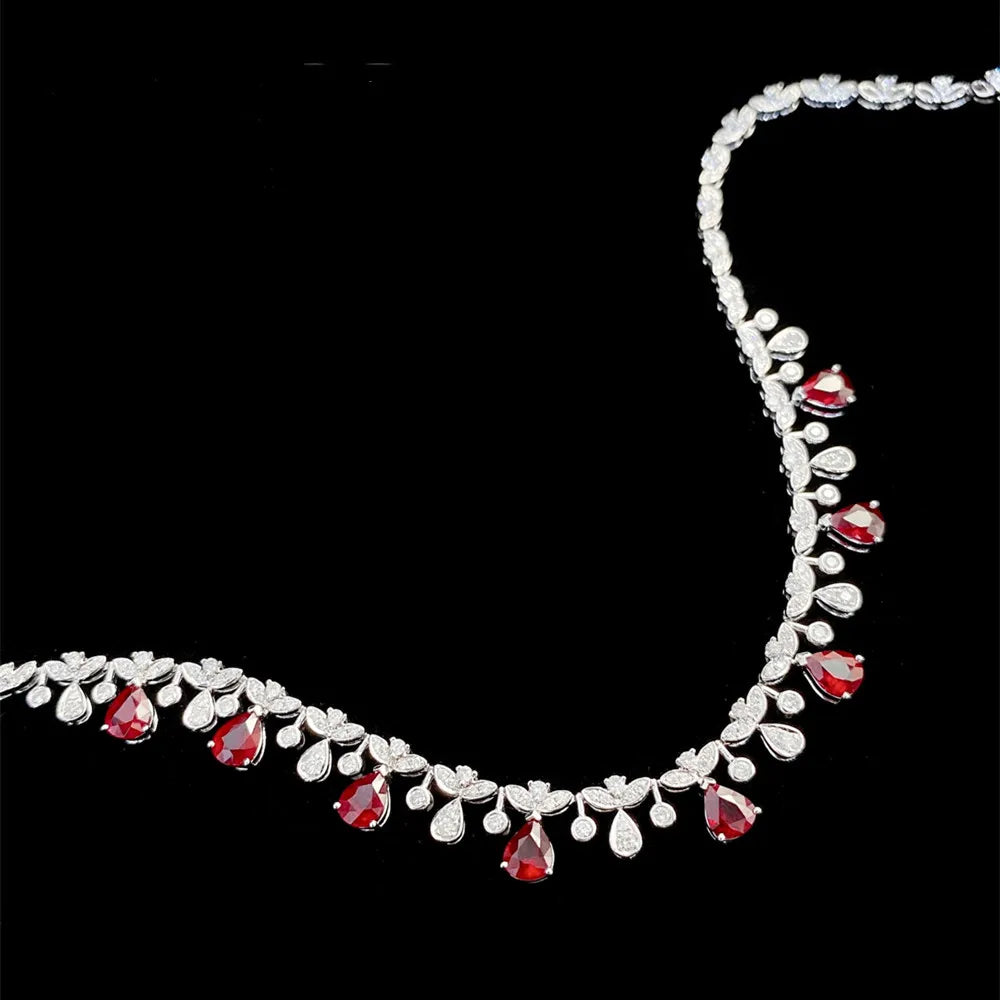 A silver-toned floral necklace featuring red teardrop-shaped gemstones and small clear stones, displayed against a solid black background.