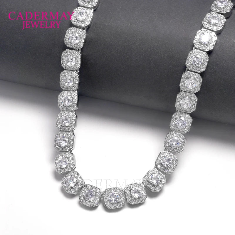 A silver-toned pave-set necklace with round and cushion-cut clear stones, displayed on a dark gray cylindrical stand against a white background. The brand name 'CADERMAY JEWELRY' is visible in pink text in the upper left corner.