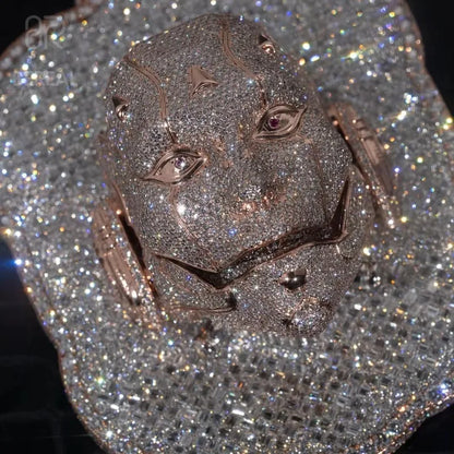 A close-up of a highly detailed, glittering lion head jewelry piece, heavily embellished with sparkling clear stones in a rose gold or pink-toned metal setting, set against a dark background.