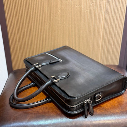 A black leather briefcase with dual top handles and silver-tone hardware, resting on a brown leather surface against a wood-paneled background.