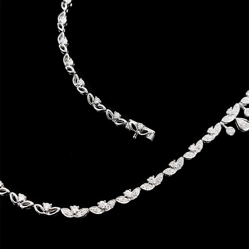 A silver tennis necklace featuring a continuous leaf and heart pattern set with clear stones, displayed against a solid black background.