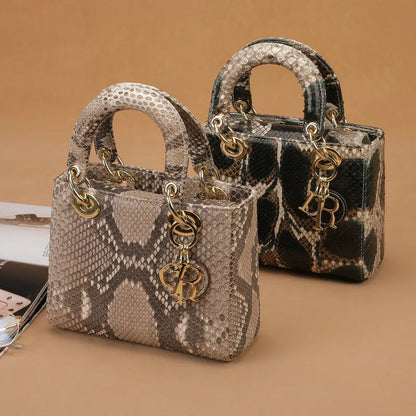 Two mini top-handle handbags with a snakeskin pattern, displayed on a warm beige background. The foreground bag is light beige and gray, while the background bag is black and beige.