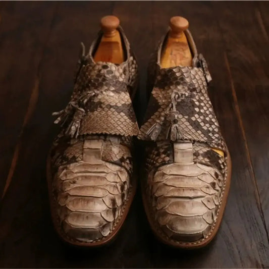 A pair of men's slip-on loafers with a textured python/snakeskin pattern in shades of brown, beige, and gray, resting on a dark wooden surface.