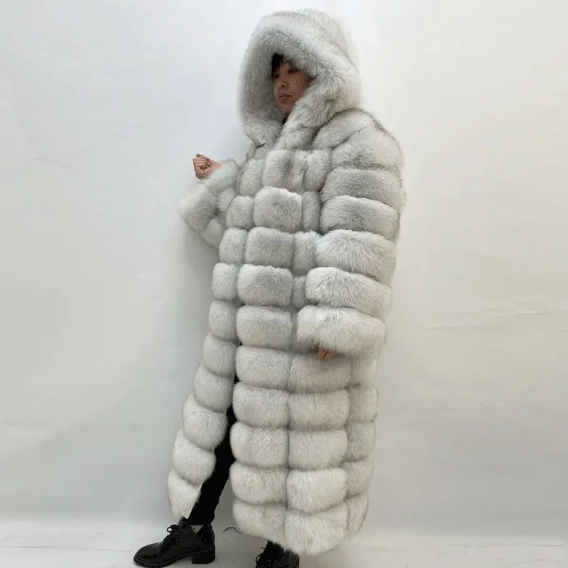 A person wearing a long, oversized hooded coat made of chunky rectangular fur or faux-fur panels. The coat is light gray to off-white with a soft, fluffy texture.