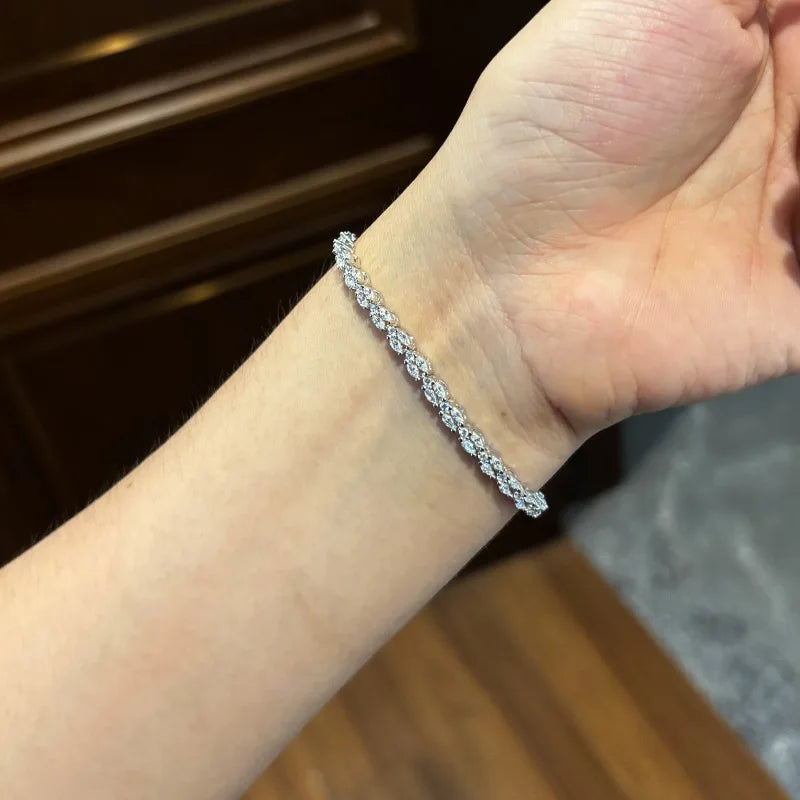 A close-up of a person's wrist wearing a silver tennis bracelet with sparkling clear stones, set against a dark wood background.
